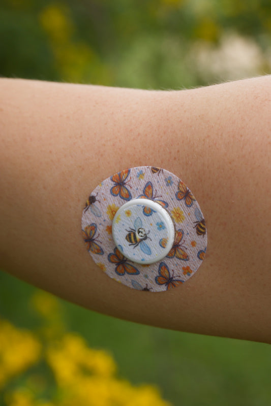 Bees and Butterflies CGM patch for FreeStyle Libre 2 — bees and butterflies with flowers on off white. Upper arm.