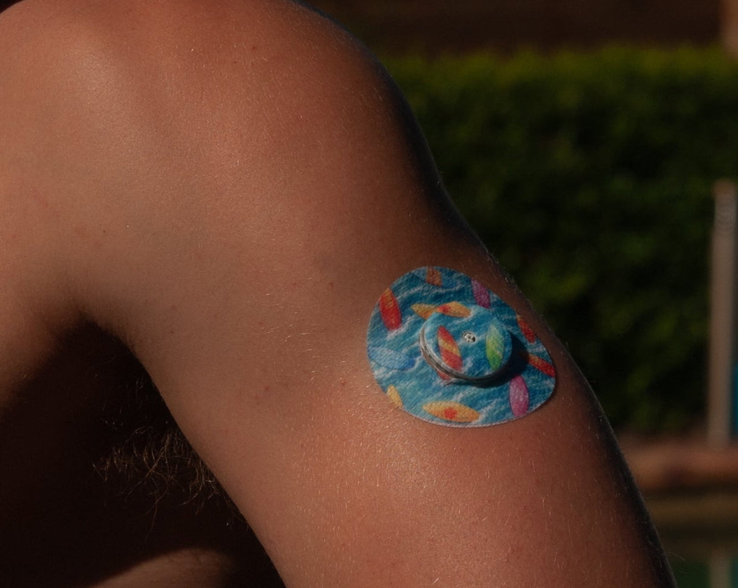 Surfboards CGM patch worn on persons upper arm for FreeStyle Libre 2 — colourful surfboards on blue waves