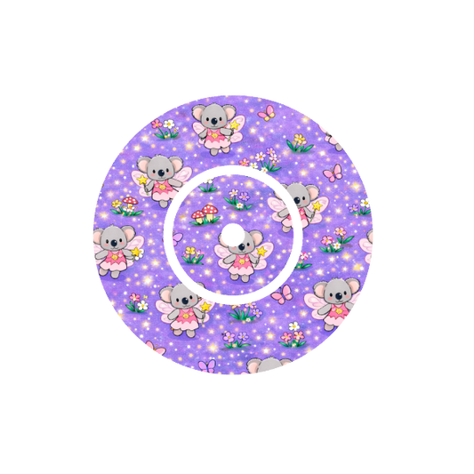 Circular shape with Binki the koala dressed as a fairy playing in a fairy garden  with mushrooms and flowers with a lilac background fits CGM FreeStyle Libre 2 device.