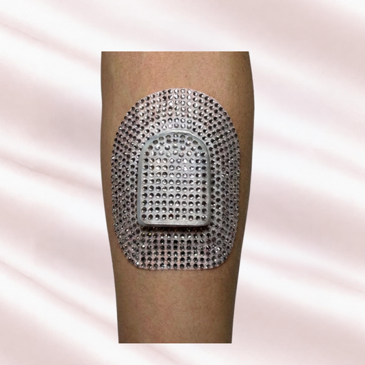 A close-up of an arm showing Omnipod Pump patch of sparkling crystal rhinestones, set against a soft, light pink satin fabric background. 